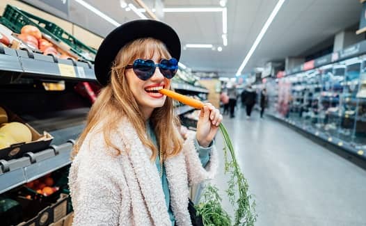 Lady with sunglasses on eating a carrot in a supermarket